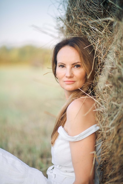 A woman in a white dress sits in a field of hay.