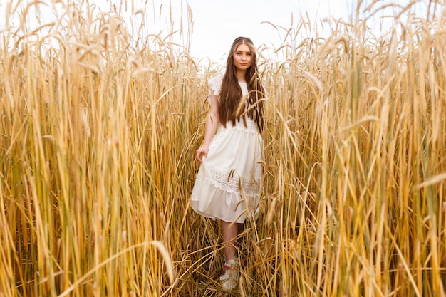 Woman in white dress standing in field with spikelets in summer