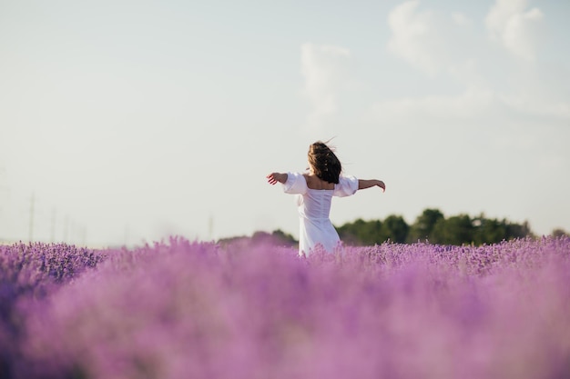 woman in white dress with hands up looking on lavender field and enjoying beautiful time a