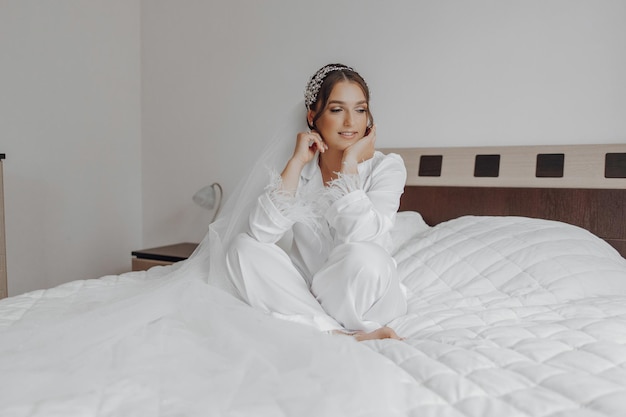 A woman in a white gown sits on a bed