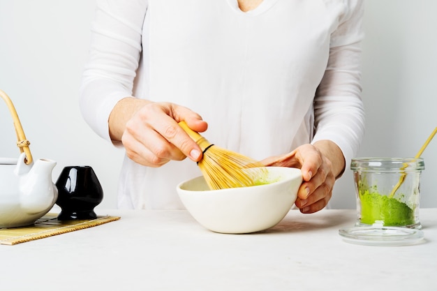 Woman in white prepare Japanese green Matcha tea by whipping it in a bowl with a bamboo Chasen whisk 