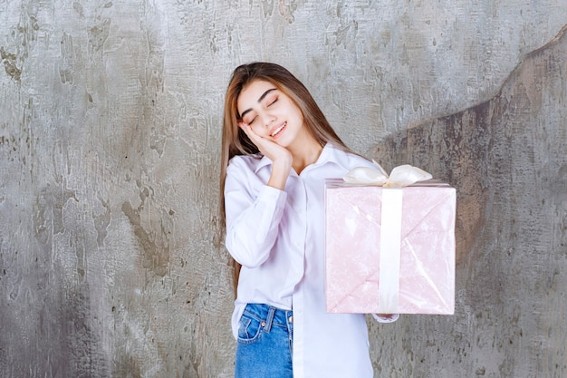 woman in white shirt holding a pink gift box wrapped with white ribbon and feeling tired and sleepy.