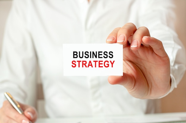 A woman in a white shirt holds a piece of paper with the text: BUSINESS STRATEGY. business concept for companies