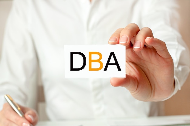 A woman in a white shirt holds a piece of paper with the text: DBA. Business concept for companies. DBA - short for doctor of business administration.