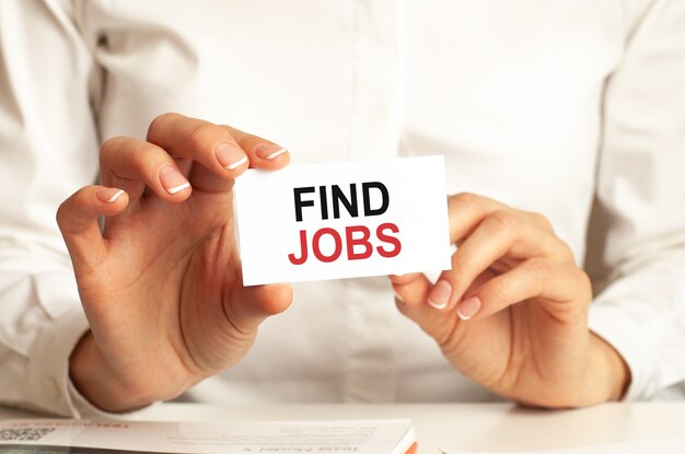 A woman in a white shirt holds a piece of paper with the text: find jobs. Business concept for companies.