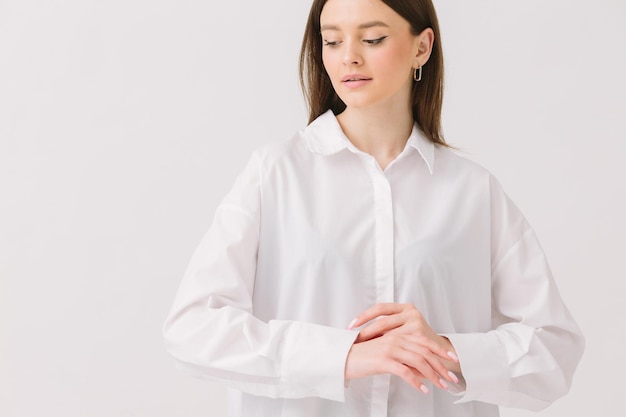 A woman in a white shirt stands in front of a white background.