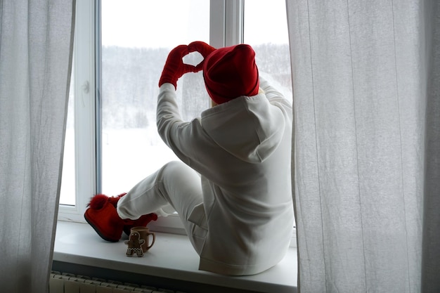 A woman in a white suit sits at a winter window