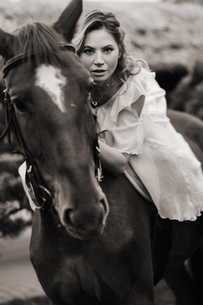 A woman in a white sundress riding a horse near a farm black and white photo