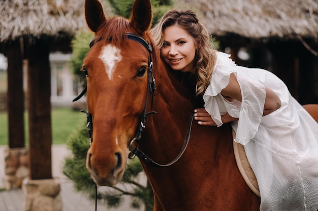 A woman in a white sundress riding a horse near a farm