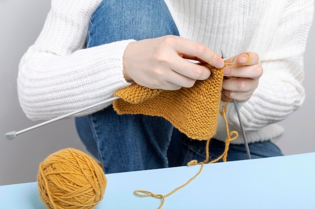 Woman in white sweater knits yellow yarn scarf