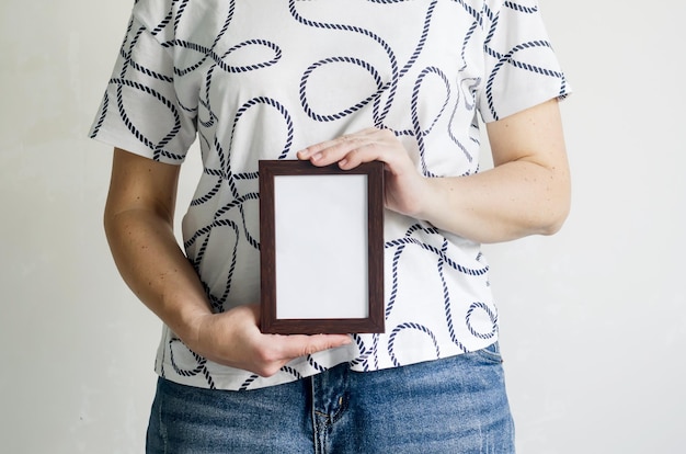 A woman in a white T shirt and jeans holds a frame in her hands