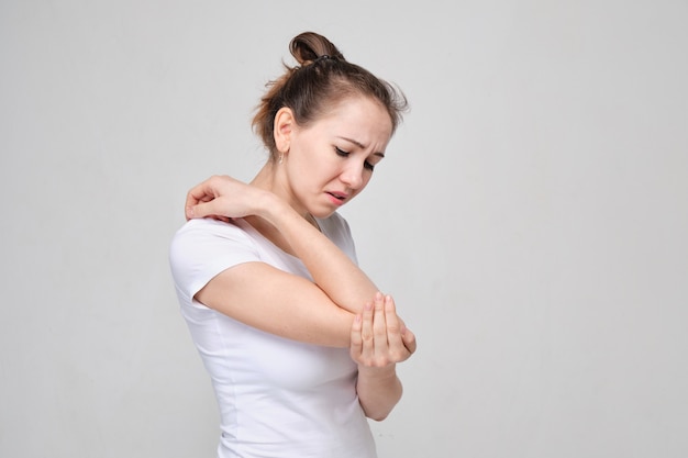 woman in white T-shirt massages her elbow from acute pain in the joint.