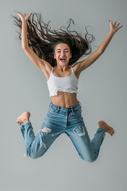 a woman in a white tank top is jumping in the air with her hair blowing in the air