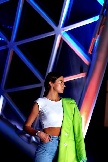 A woman in a white top and a green scarf is standing in front of a building.