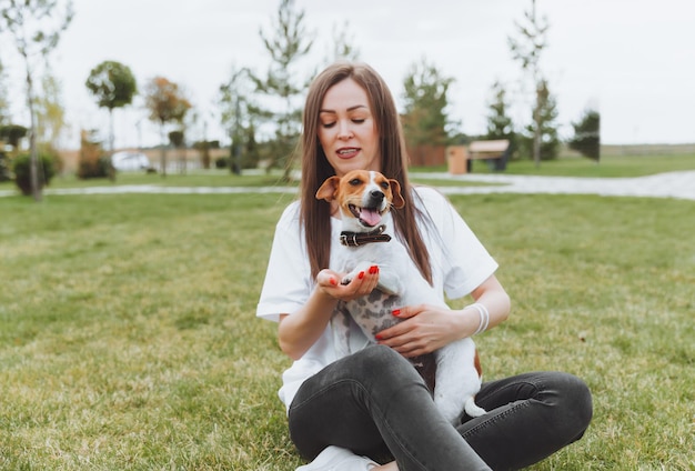 A woman in a white Tshirt and jeans hugs her Jack Russell Terrier dog in nature in the park Loyal best friends since childhood Lifestyle