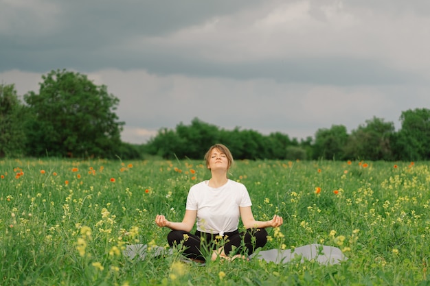 Woman in a white tshirt and leggings doing yoga in a beautiful field on a sports mat lifestyle 