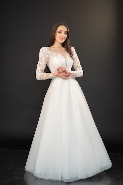 A woman in a white wedding dress stands in front of a black background.