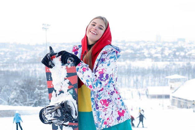 Woman winter outdoor snowboarding concept. Young woman holding snowboard on her shoulders, she's looking away and smiling, copy space, close up