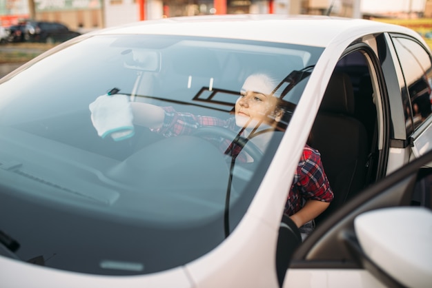 Woman wipes the windshield of the car from the inside