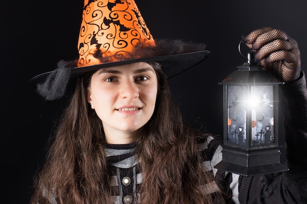 A woman in a witch costume holds a glowing lantern