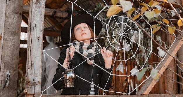 Woman in witch halloween masquerade costume with spooky face pretending to be stuck in spiderweb