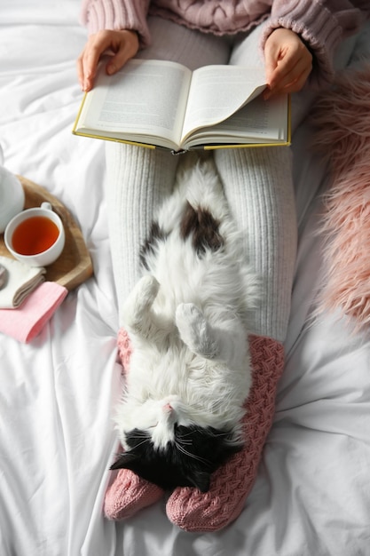 Woman with adorable cat reading book on bed view from above