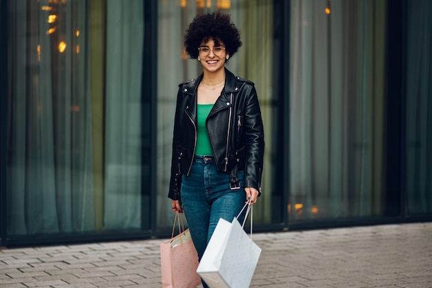 Woman with afro hair holding shopping bags while walking on the street