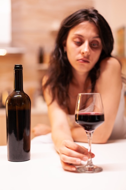 Woman with alcohol addiction holding hand on glass of red wine being disappointed and sad. Unhappy person disease and anxiety feeling exhausted with having alcoholism problems.