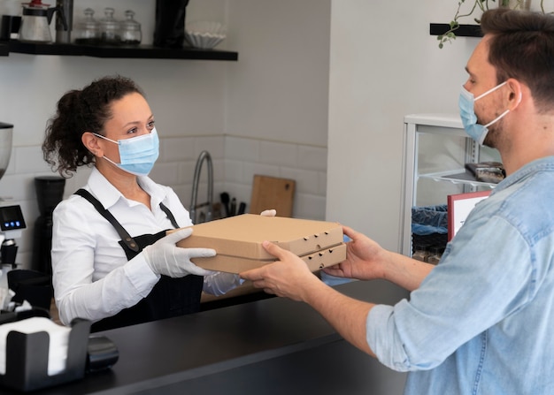 Woman with apron offering packed takeaway food to male customer