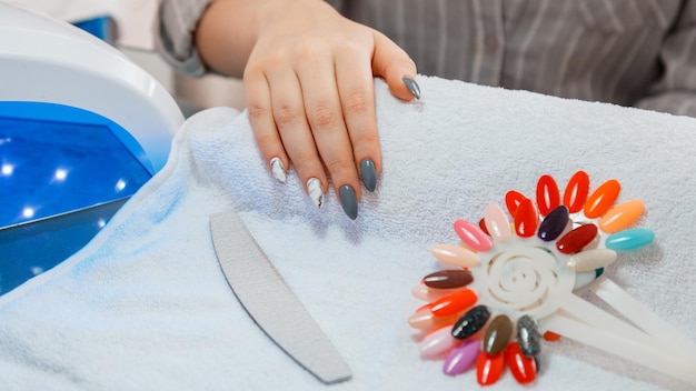 Woman with artificial acrylic nails picks up new polish color during manicure procedure Manicure process in beauty salon on white towel Hygiene beauty of hands in nail salon Long web banner