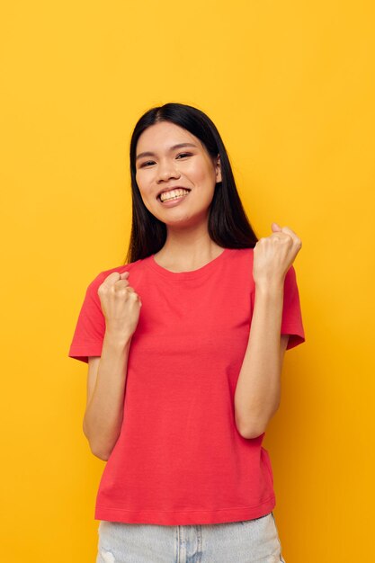 Woman with asian appearance in a red tshirt posing emotions fun yellow background unaltered