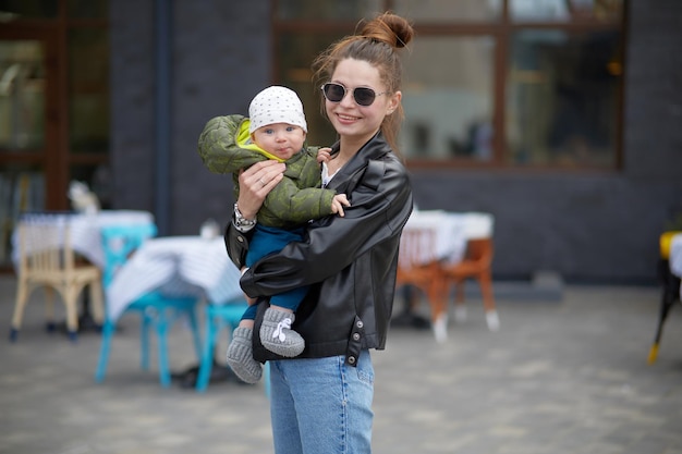 A woman with a baby in a black jacket and jeans stands in front of a cafe