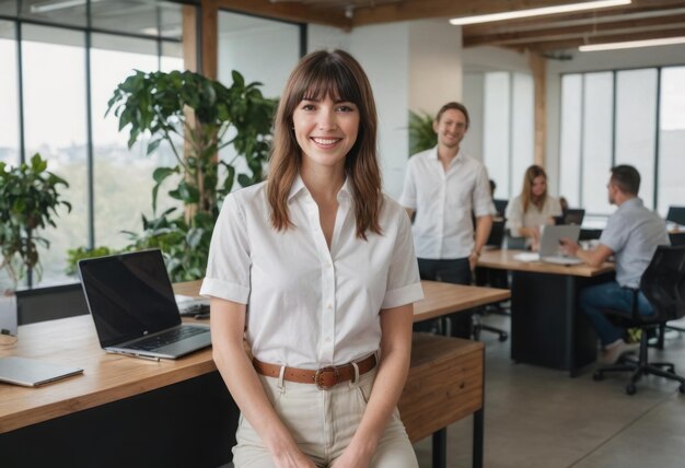 A woman with bangs stands smiling at the office colleagues are collaborating in the background