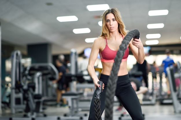 Woman with battle ropes exercise in the fitness gym.