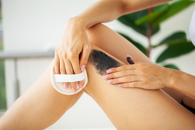 Woman with beautiful skin on her feet applies anti-cellulite scrub cream on her leg