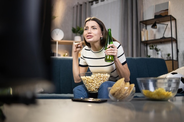 Woman with beer and snacks watching soccer match on TV