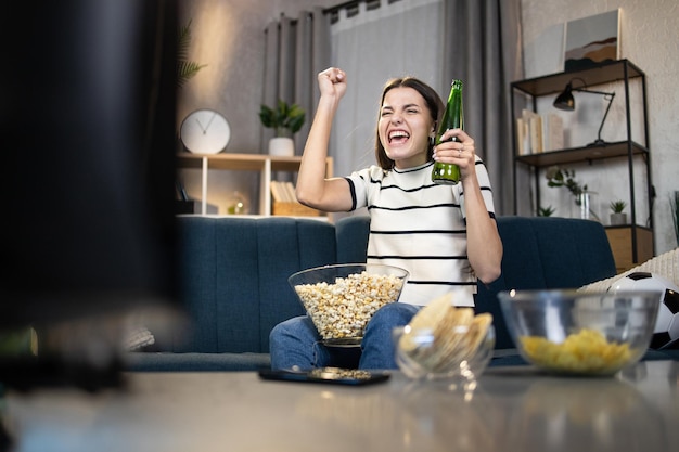 Woman with beer and snacks watching soccer match on TV