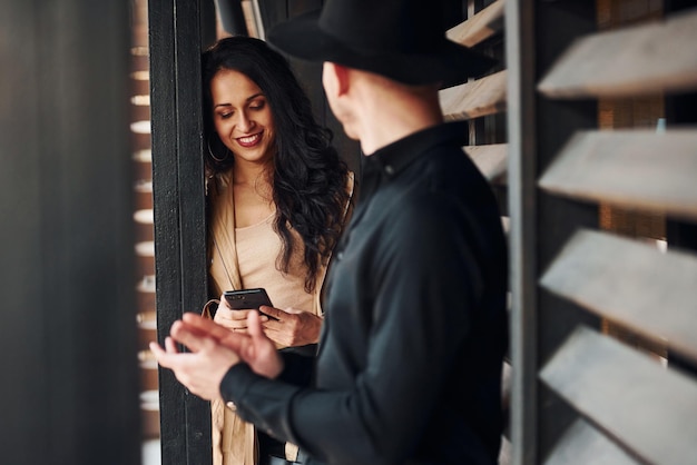 Woman with black curly hair and her man standing together near wooden windows