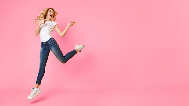 A woman with blonde hair is jumping and pointing towards the right side of the image while smiling