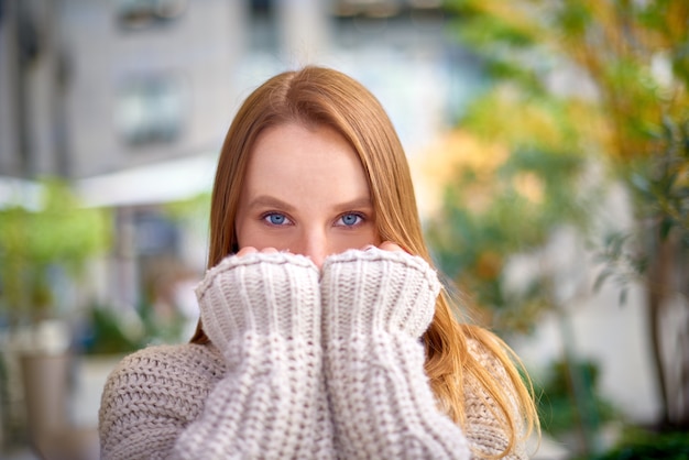 Woman with blue eyes in warm chunky knit sweater covers her mouth with hands