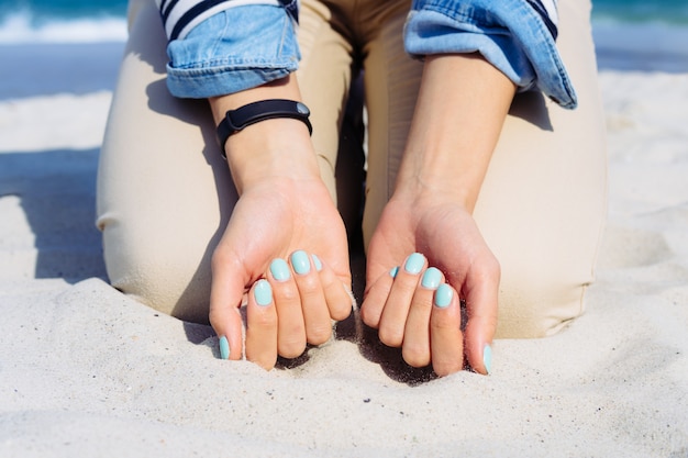 Woman with blue nail polish on hands sitting on the beach sand