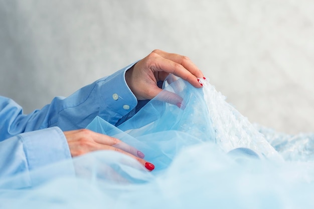 Woman with blue satin fabric with threads on a wooden background with beads