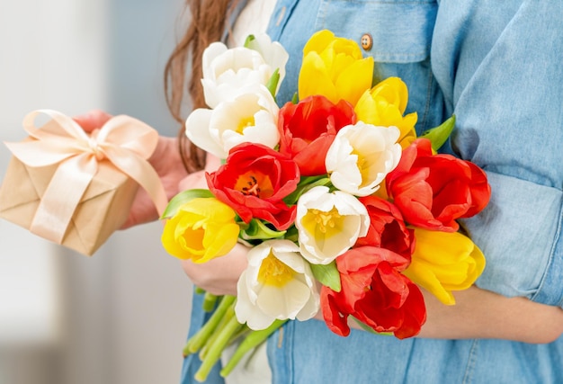 Woman with a bouquet of tulips and a gift box in her hands closeup