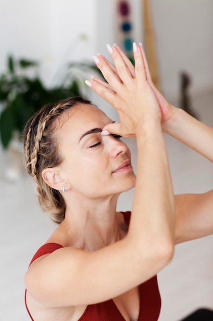 A woman with braids in her hair is doing Anjali Mudra in a yoga studio