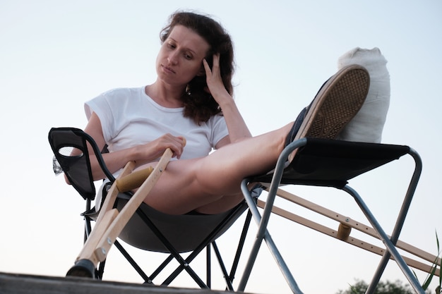 Woman with broken in cast is sitting on chair in nature Leg injury Rehabilitation after a fracture