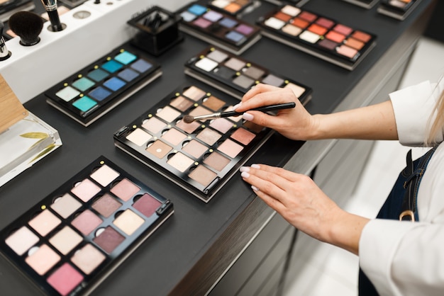 Woman with brush choosing shadows in cosmetics store. Buyer in luxury beauty shop salon, female customer in fashion market