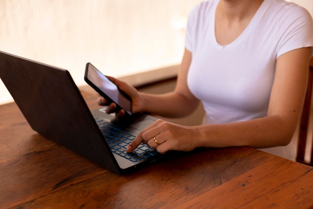 Woman with cellphone in hand and typing on laptop home Office