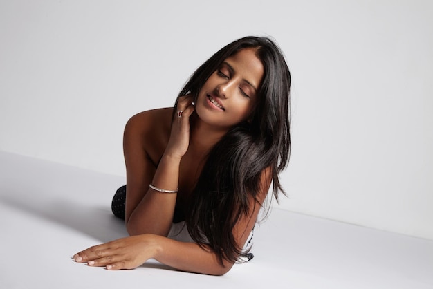 Woman with closed eyes lies down on white floor in studio