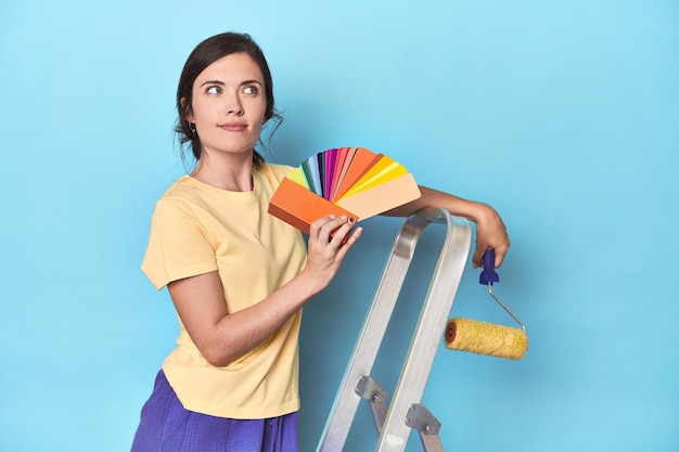 Woman with color palette painting wall on ladder