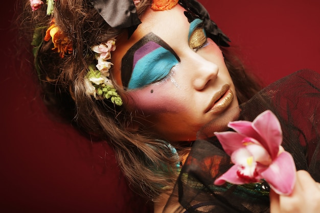 Woman with creative make up holding pink flower